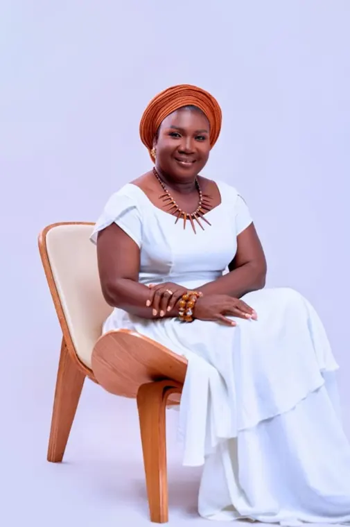 Sika Coleman seated in a white dress and orange headwrap