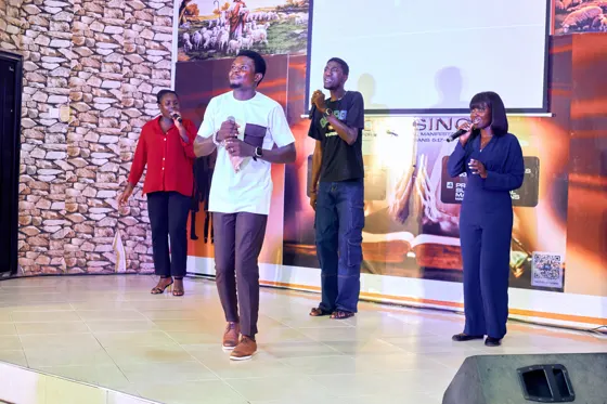 A man in a white shirt holding a microphone with singers behind him on stage