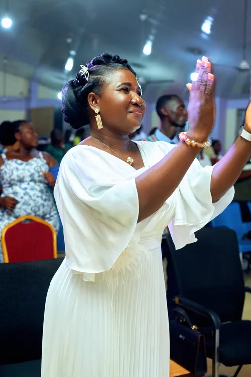 A woman in a white dress raising her hand during worship