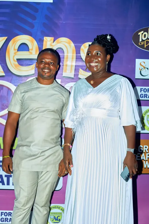 Two attendees smiling in front of the Tokens of Praise backdrop