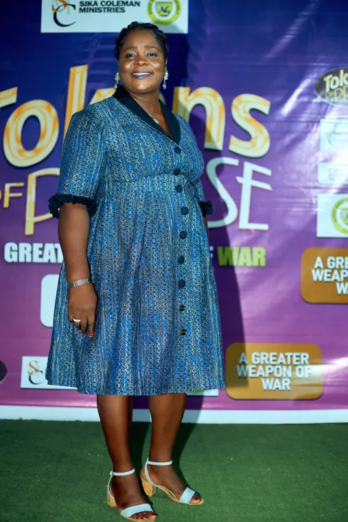 An attendee in a blue dress standing in front of the Tokens of Praise backdrop